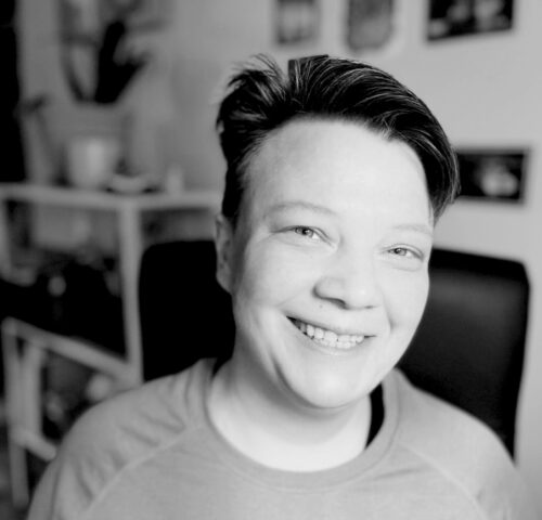 A black and white portrait of Lucky, a short-haired person, smiling at the camera.